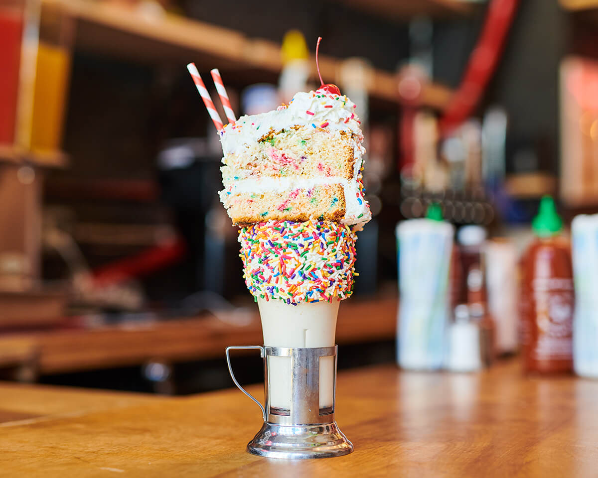 Black Tap Craft Burgers & Shakes - This cake shake provides you a generous dose of vanilla frosted rim with rainbow sprinkles topped with a slice of luscious cake, cherry and whipped cream – this milkshake is sure to bring all the boys to the yard!