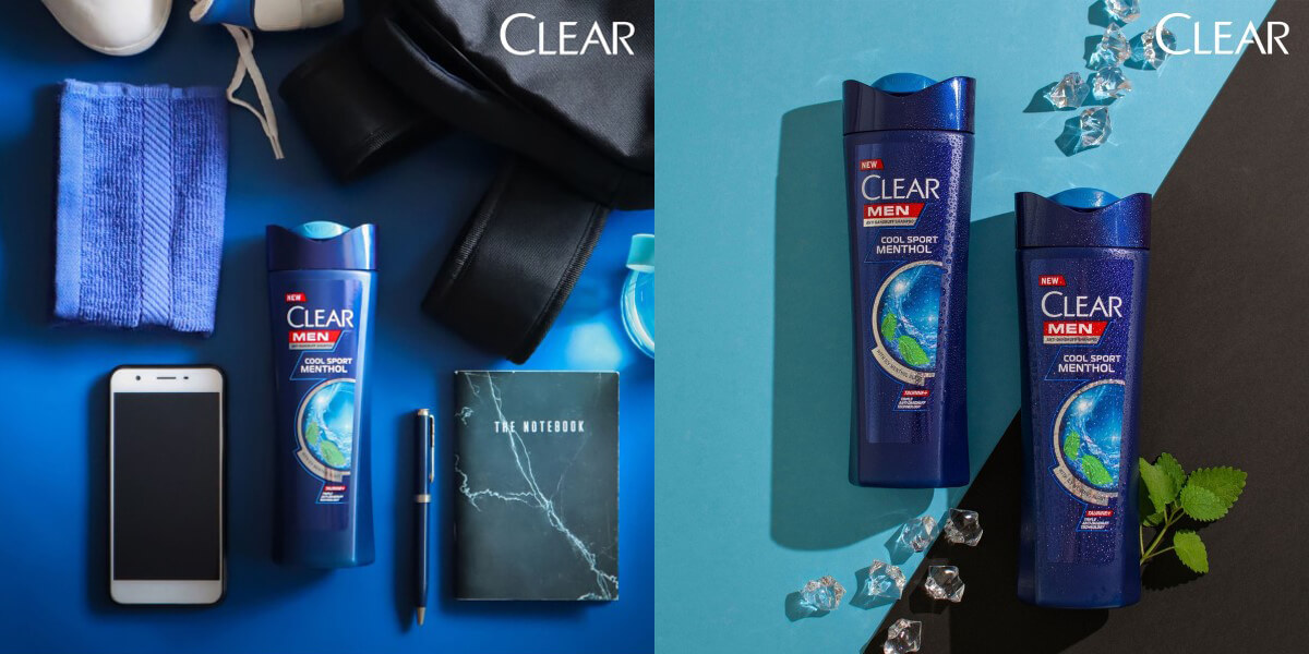 A bottle of Clear Men cool Sport Menthol Shampoo with a blue background, with items that men generally uses like handphone, bag and notebook, Two bottles of Clear Men shampoo amidst a blue and grey background, with ice and mint leaves alongside it.