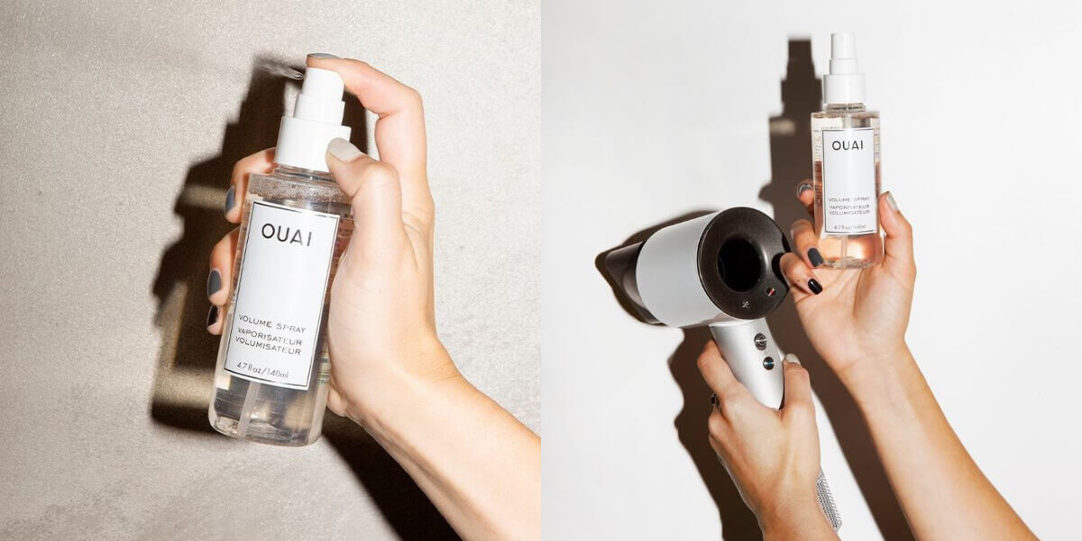 A hand holding a bottle of Ouai hair spray amidst a white background, using flash camera, A hand holding Ouai volume hairspray, and the other hand hodling a hair dryer